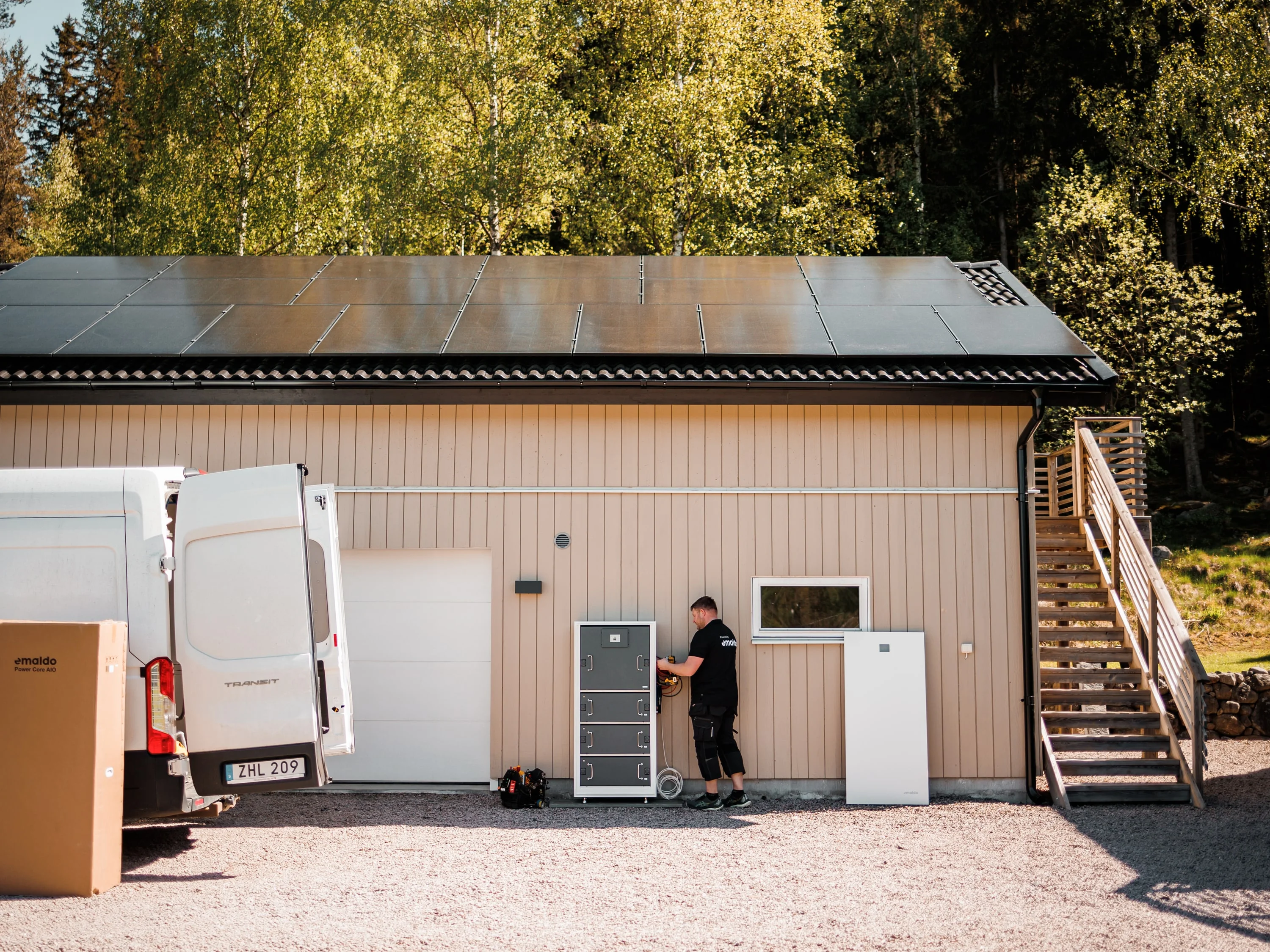 Montör vid batteriskåp utanför en byggnad med solceller på taket